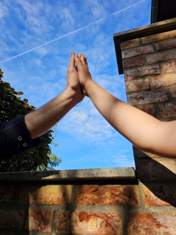 Hände treffen sich, im Hintergrund ist der blaue Himmel.